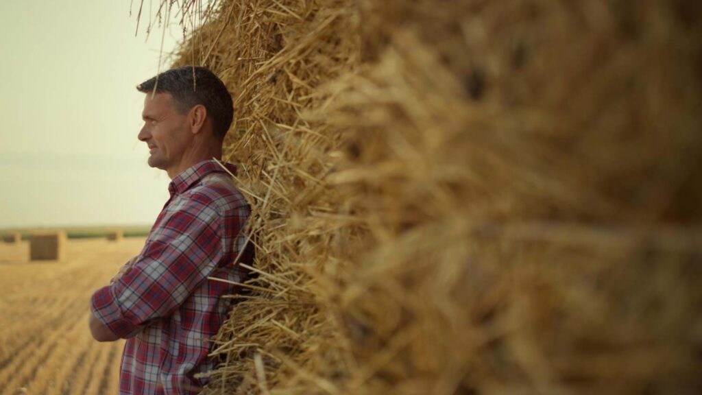 Farmer leaning against large hay bale.